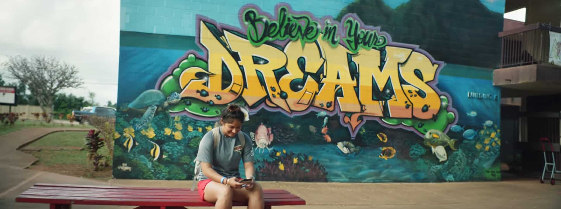 07 Invisalign Student Atheletes FEATURED Person standing in front of large yellow "Dreams" graffiti mural on blue wall outdoors.