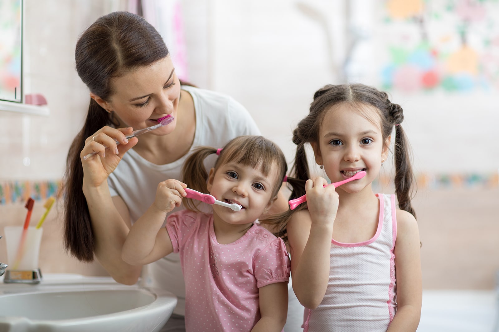 Adult woman teaching two young girls proper toothbrushing technique in bright dental clinic setting.