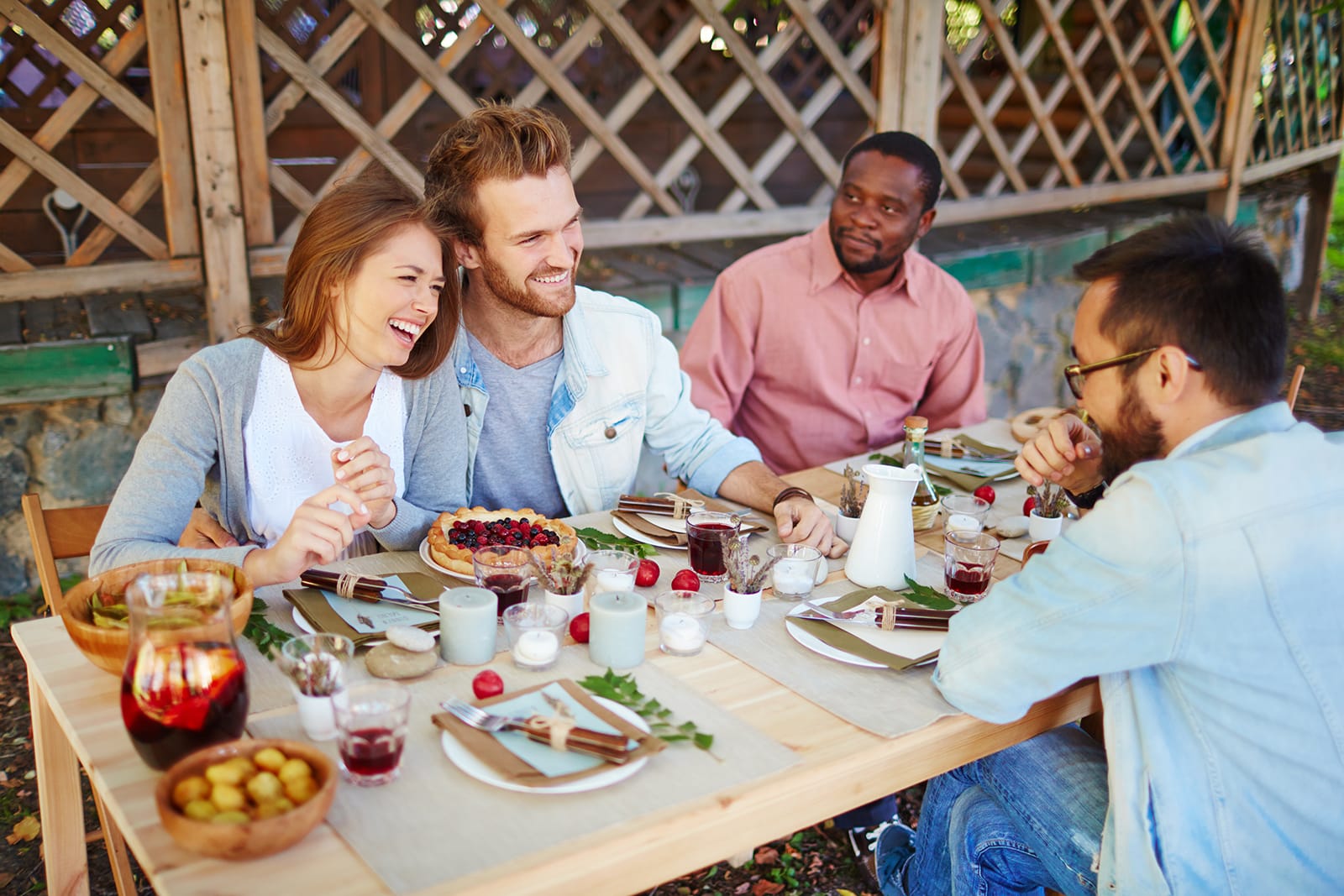 Four people enjoying a meal together at an outdoor table in a garden setting.