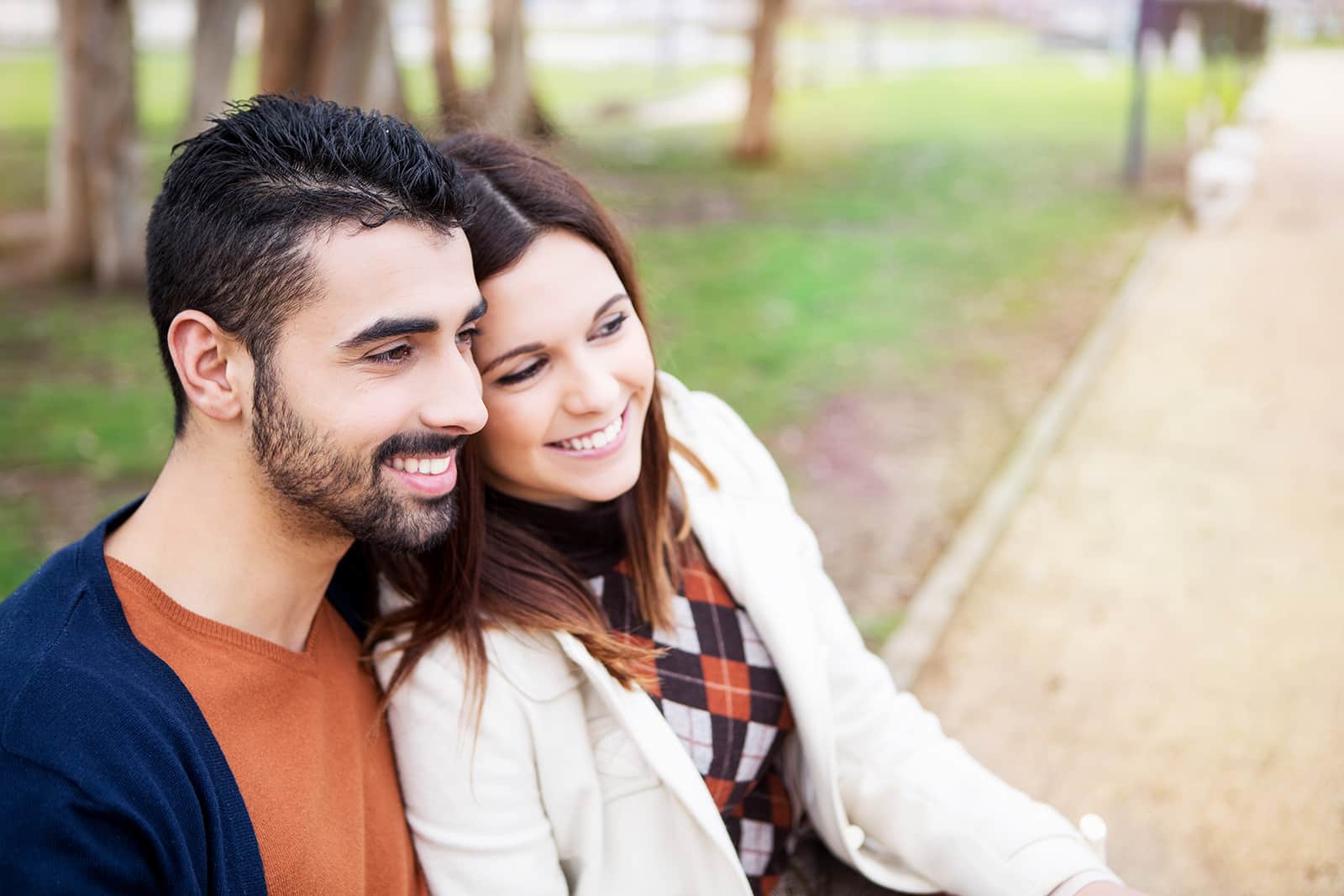 Happy couple smiling outdoors in casual clothing, relaxed park setting.