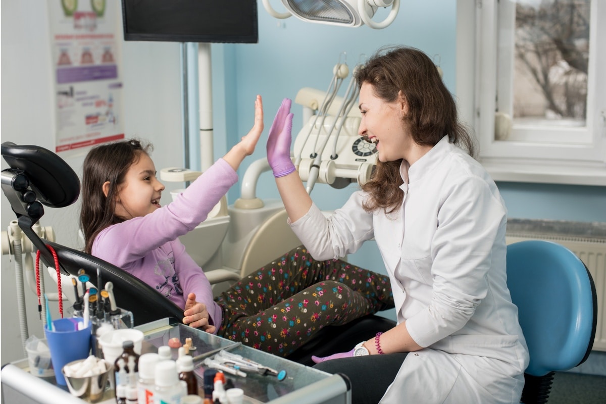 Pediatric dentist high-fiving young patient in modern dental office treatment room.