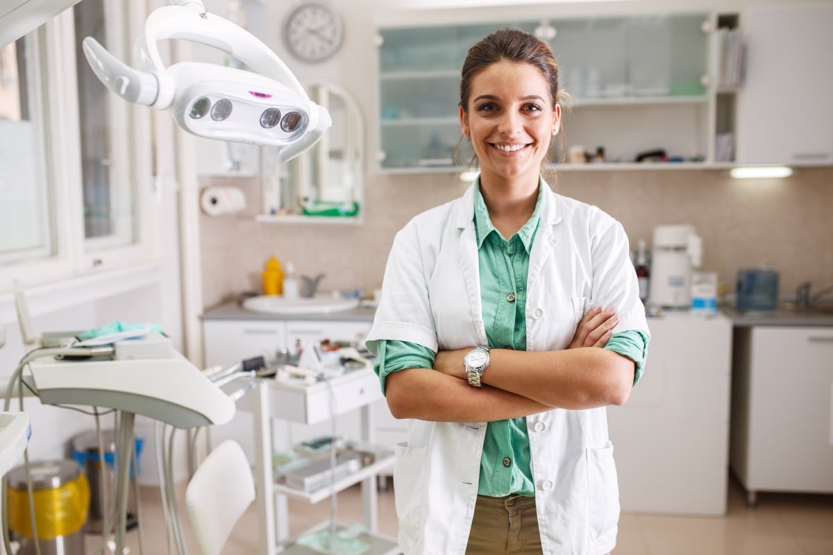 Female dentist in white coat standing confidently in modern dental clinic office.