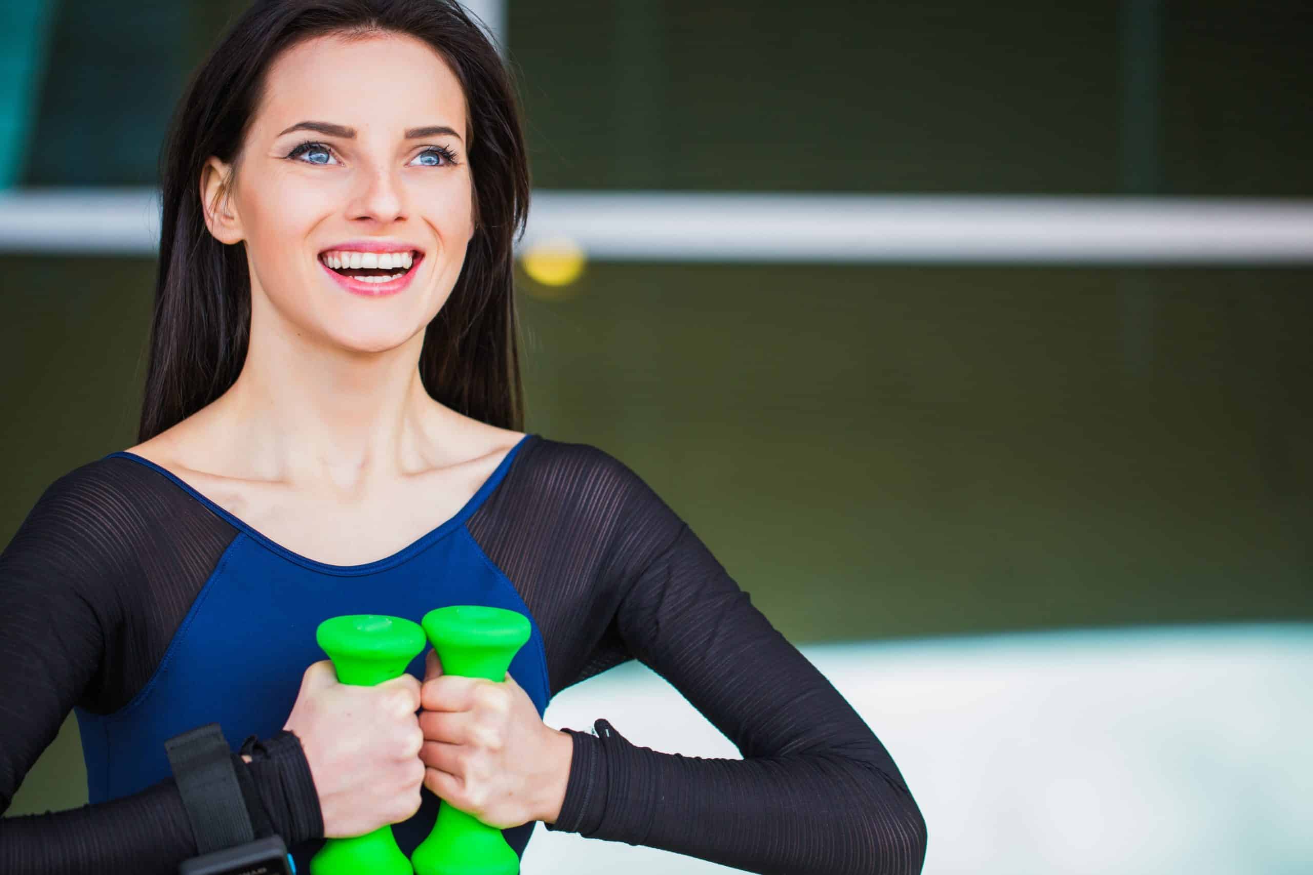 Woman in blue and black shirt holding green dumbbells in modern dental office setting.