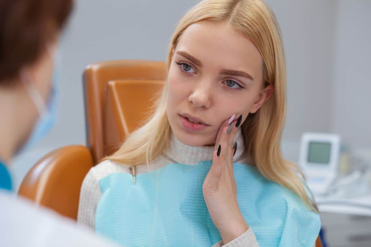 Young woman in dental chair touching her cheek during consultation with dentist in modern office.