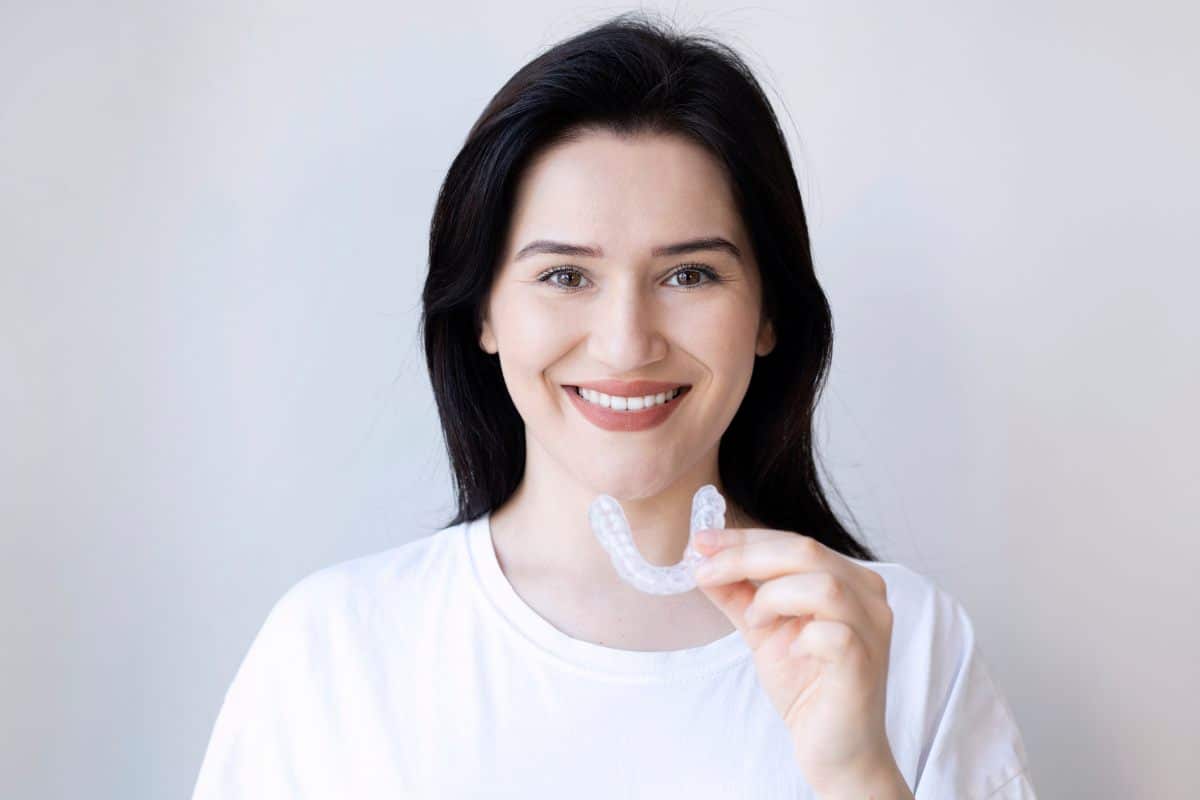 How to Stop Clenching Your Jaw Smiling woman in white shirt against neutral background for dental practice website