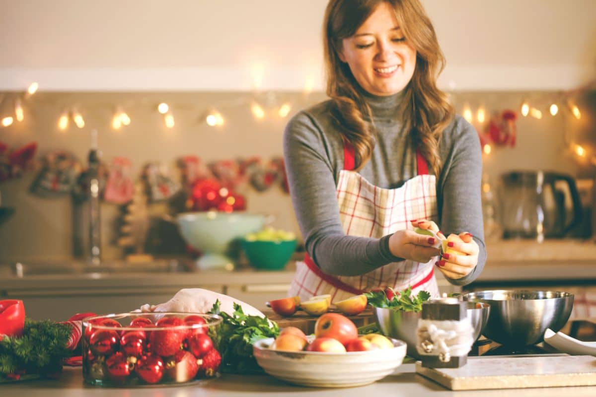 Holiday-Treats-Without-the-Sweets Woman preparing healthy food in festive kitchen decorated with holiday ornaments and garland.