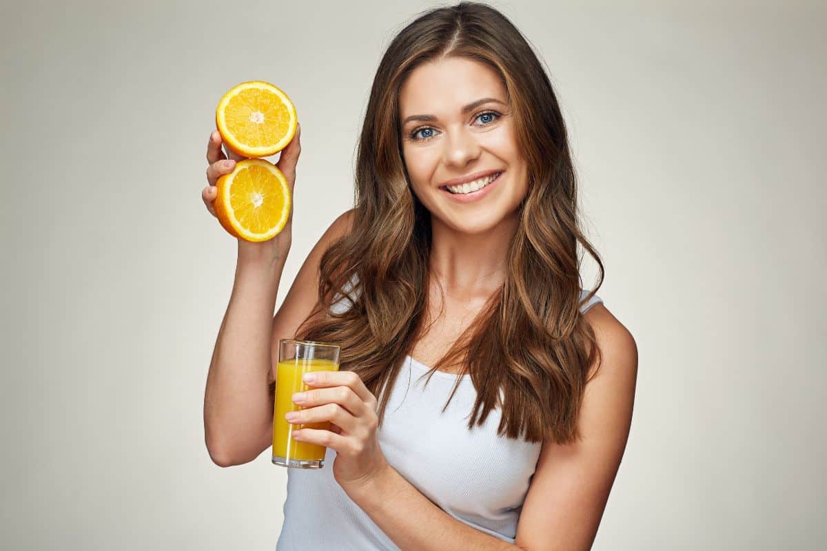 Woman holding orange slices and juice glass, promoting healthy teeth and wellness for dental care.